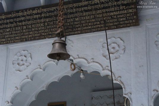 Old information board and a bell hanging inside Mirabai Temple.
