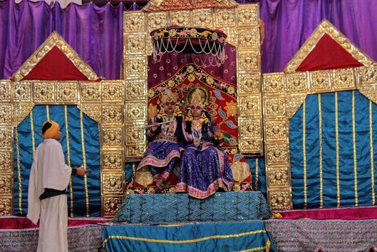 Distant darshan of Shri Radha Krishna seated on throne in blue attire at Raas Leela Moments, Vrindavan