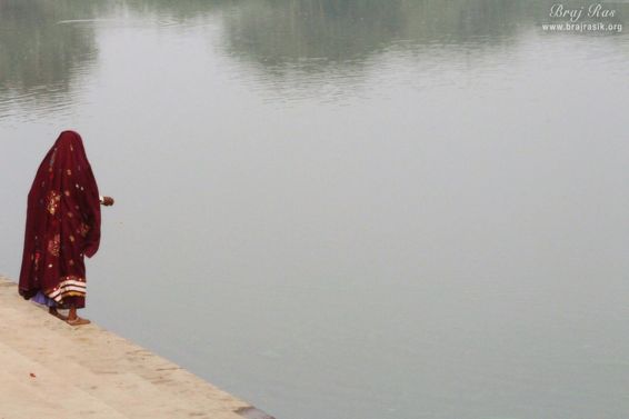 A devotee throwing food for ducks and fish in Deha Kunda, Braj