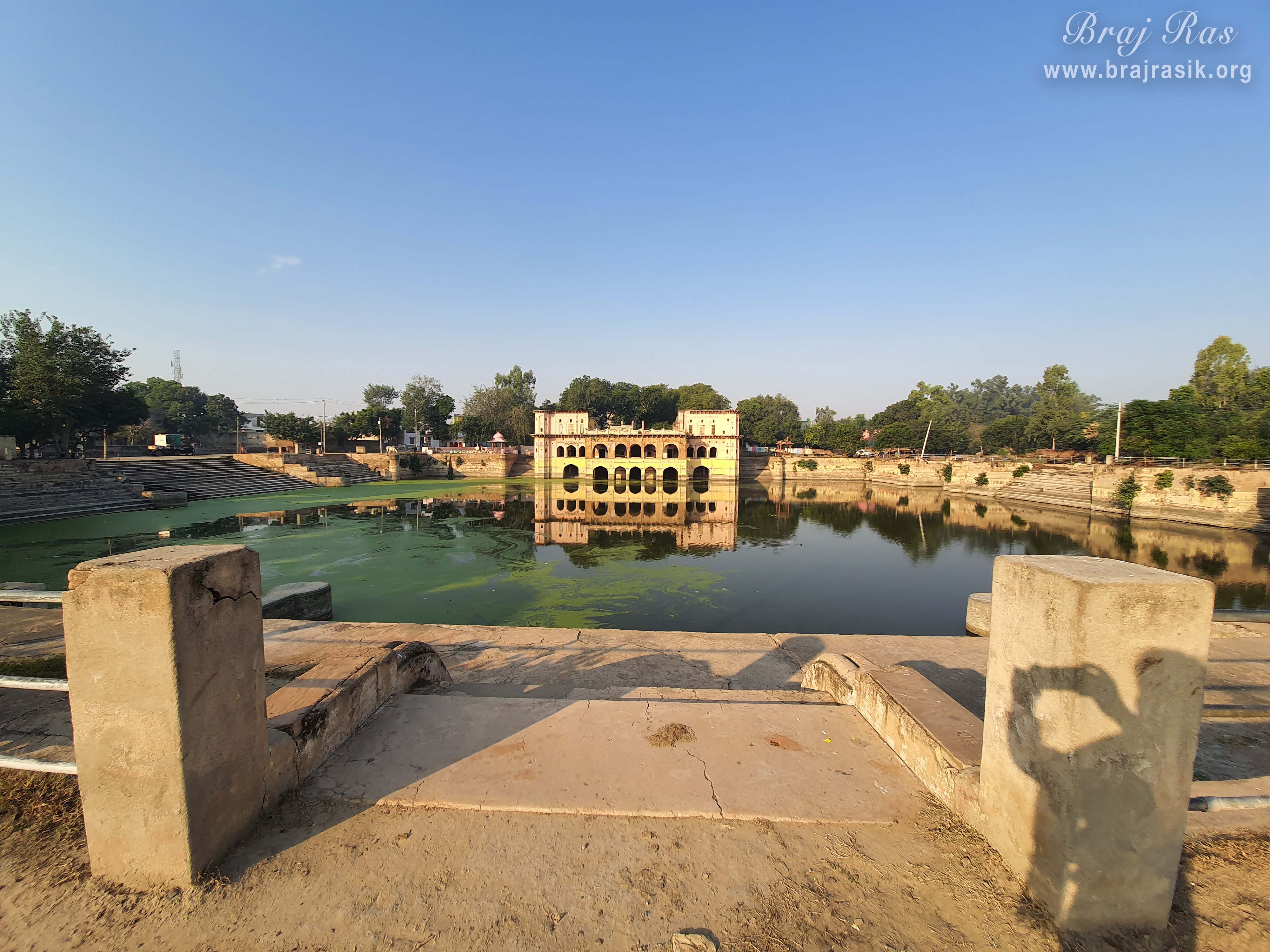 A Front full view of Sri Vrishbhanu Kund (Jal Mahal), Barsana surrounded by trees all around.